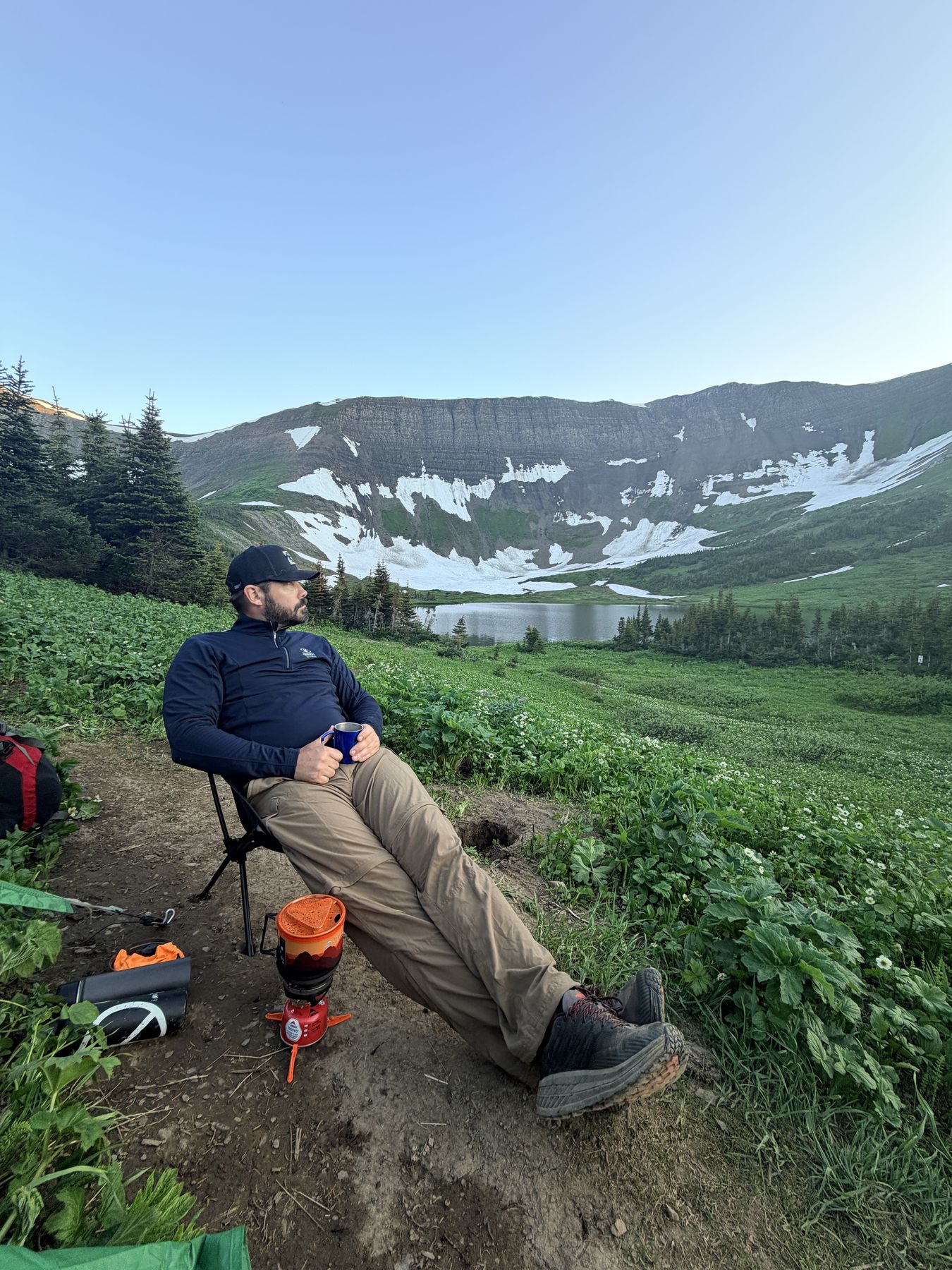 Ryan relaxing in a camp chair at the Windfall Lake campsite, looking out over the lake and the headwall