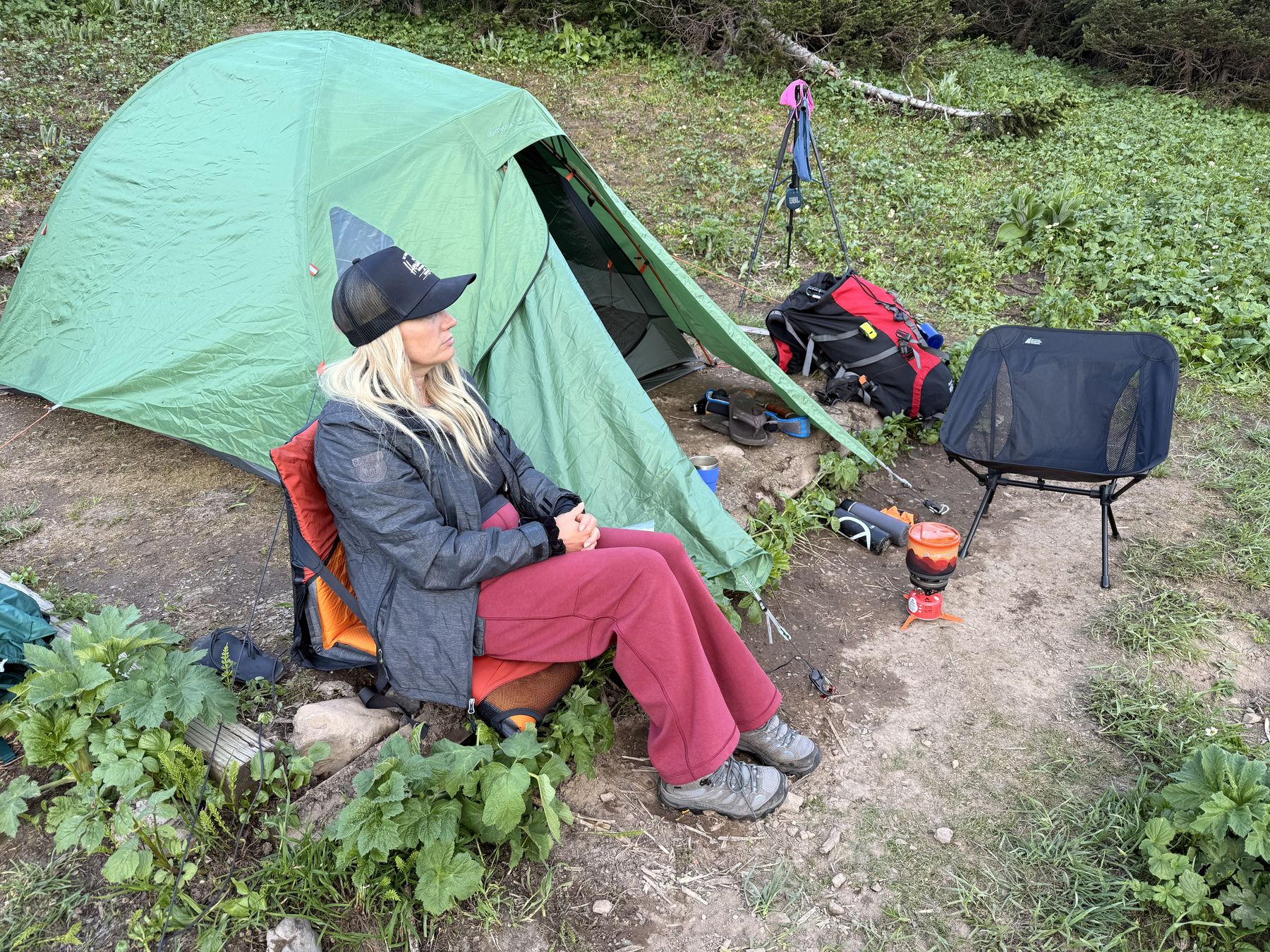 Stacie relaxing in a camp chair beside the tent and stove at the Windfall Lake campsite