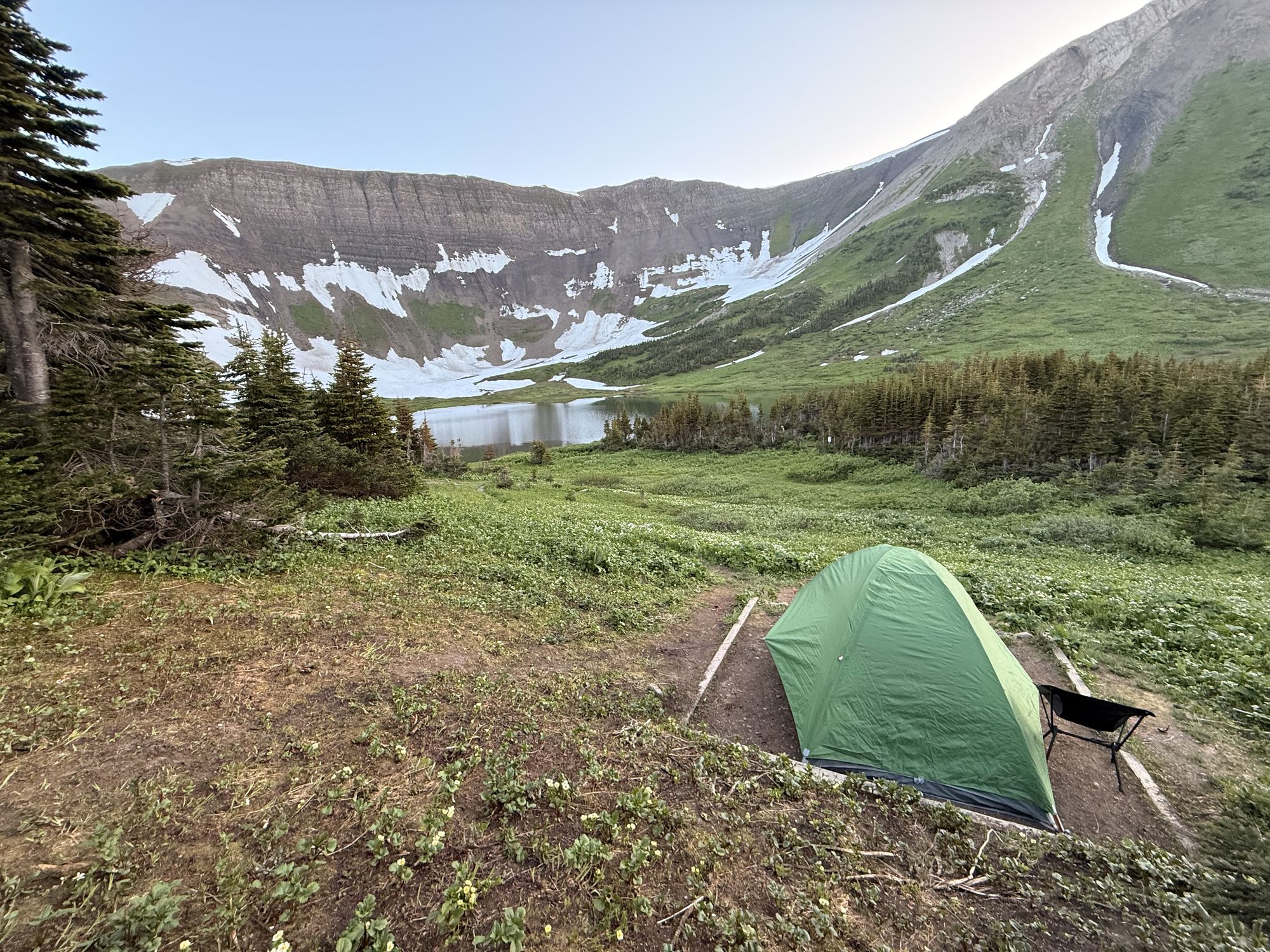 A green backpacking tent on a tent pad in the meadow at Windfall Lake, with the lake and the ridge behind
